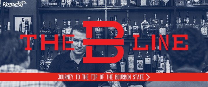 Bartender and bar stocked with bourbon with the text The B Line Journey to the Tip of the Bourbon State
